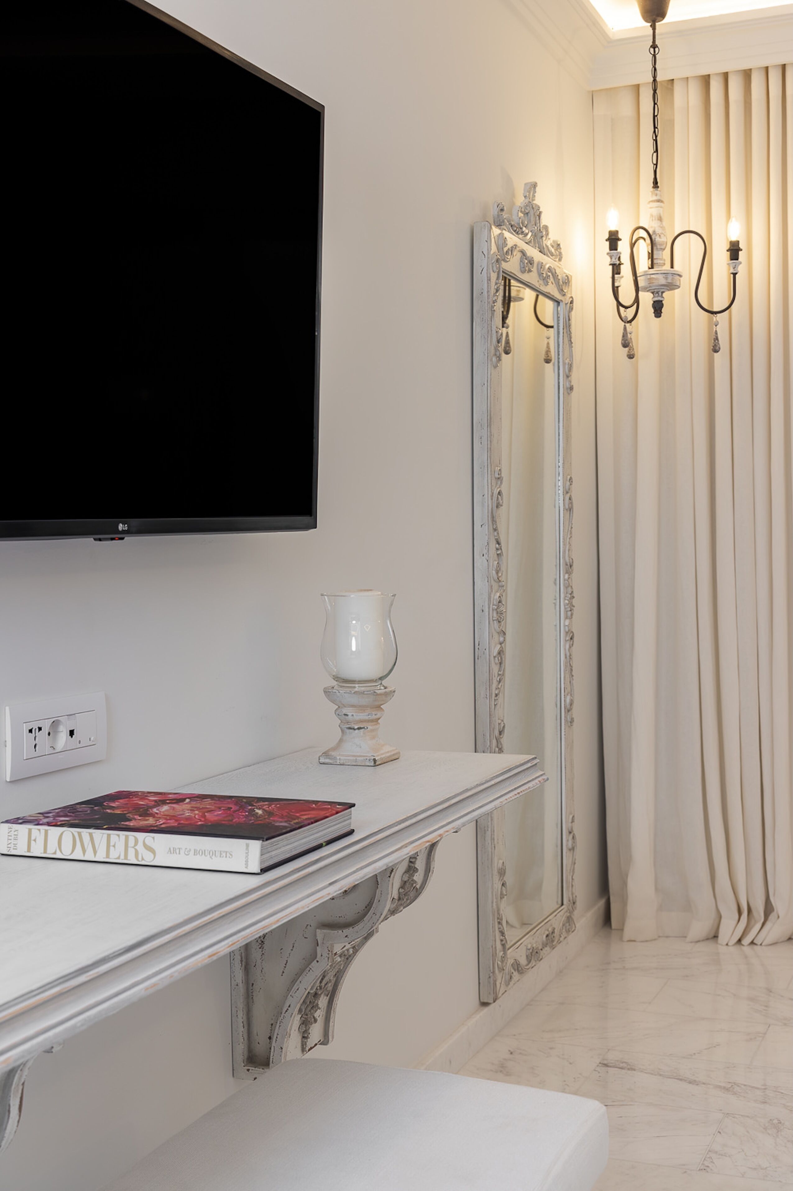 A modern living room with a flat-screen TV mounted on the wall, a white console table with a book, a candle, and a mirror.
