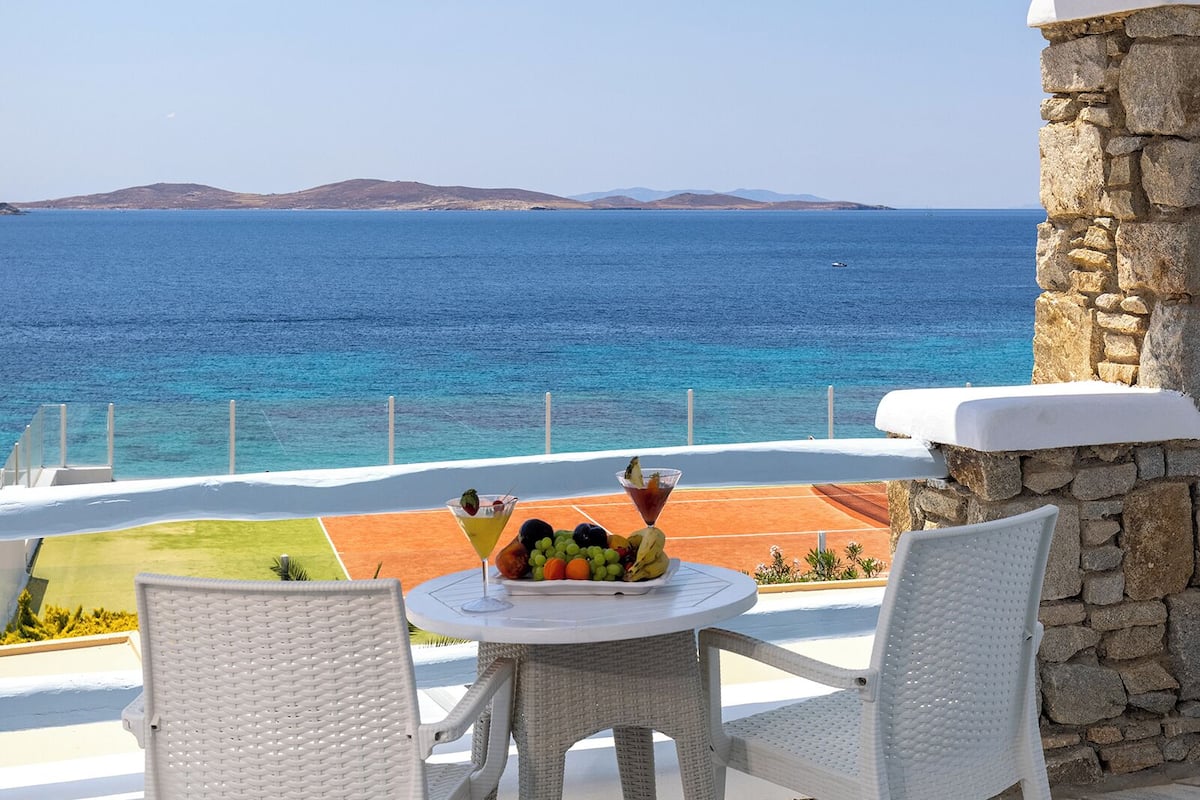 Un espace extérieur abrité, avec une table et des chaises, offrant une vue sur une mer d’un bleu profond et sur la côte lointaine.