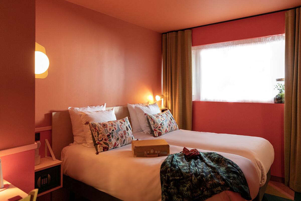 A hotel room with a bed, bedside tables, a lamp, and a window with curtains.