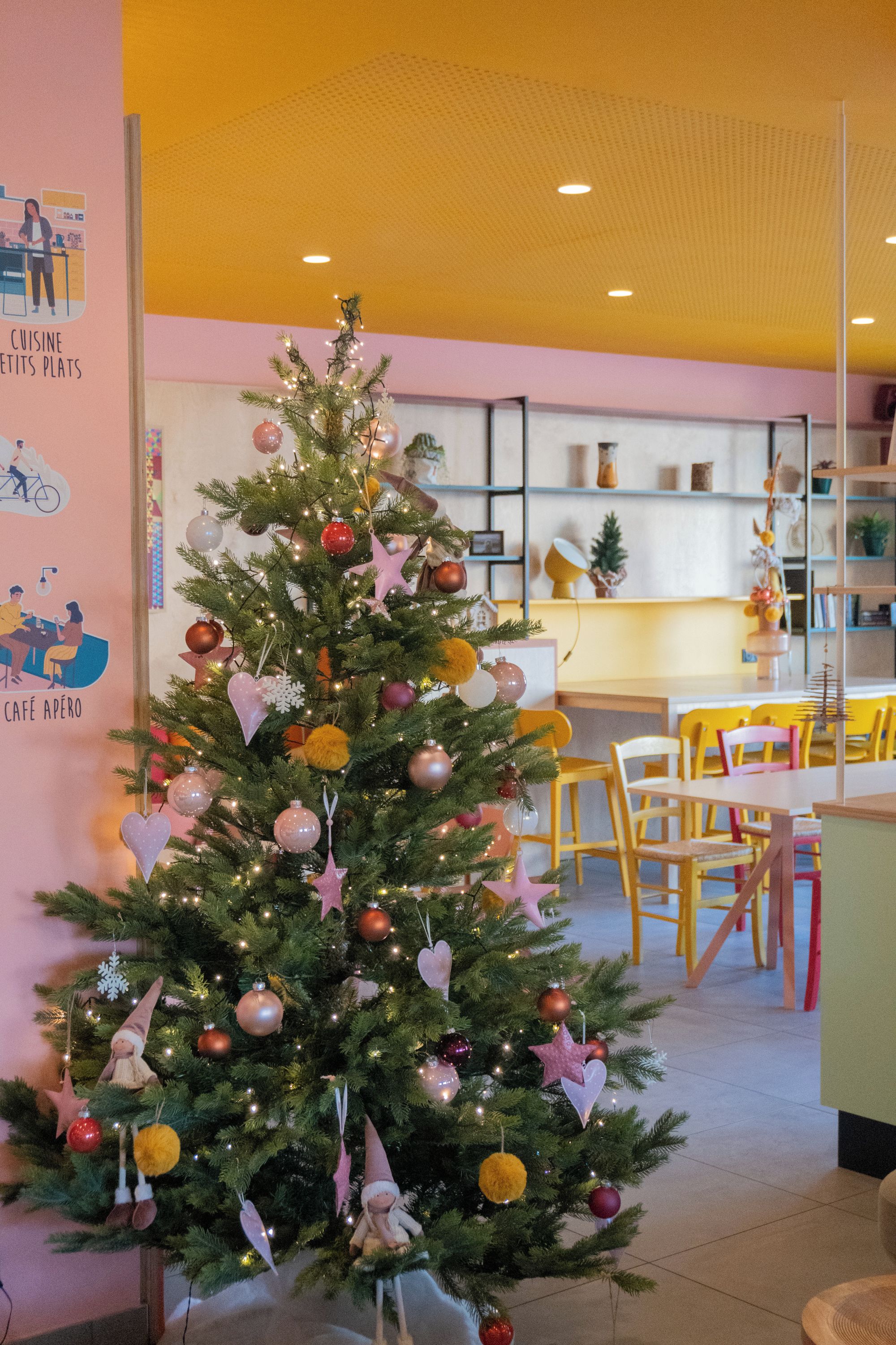 A Christmas tree decorated with ornaments and lights in a room with a yellow ceiling and a dining area in the background.
