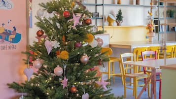 A Christmas tree decorated with ornaments and lights in a room with a yellow ceiling and a dining area in the background.