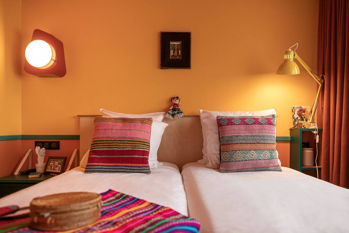 A hotel room with a bed, pillows, a nightstand, a lamp, and a wall-mounted picture.