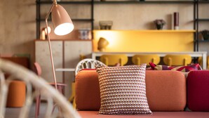 A cozy living room with a sofa, a patterned pillow, a floor lamp, and a bookshelf in the background. - Paul & Pia By Stay Collection (Colmar)