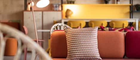 A cozy living room with a sofa, a patterned pillow, a floor lamp, and a bookshelf in the background.