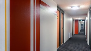 A hotel corridor with striped walls, a carpeted floor, and doors leading to rooms. - Hôtel Inn Dijon-Quetigny (Quetigny)