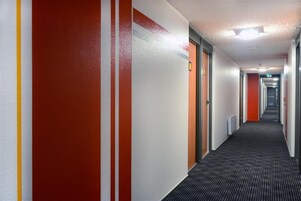 Corredor de hotel com paredes listradas, piso coberto de carpete e portas que dão para quartos.
