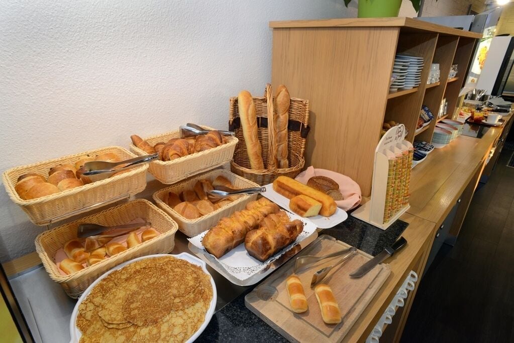 A breakfast buffet with various breads, pastries, and a large plate of pancakes.