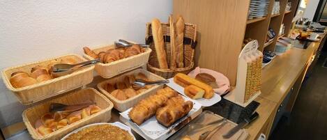 A breakfast buffet with various breads, pastries, and a large plate of pancakes.