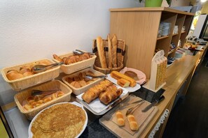 A breakfast buffet with various breads, pastries, and a large plate of pancakes. - Hôtel Inn Dijon-Quetigny (Quetigny)