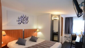 A hotel room with a large bed, two bedside tables with lamps, a flat-screen TV mounted on the wall, a desk with a chair, and a mirror. - Hôtel Inn Dijon-Quetigny (Quetigny)