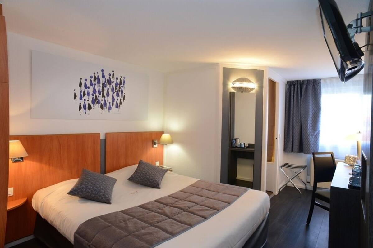 A hotel room with a large bed, two bedside tables with lamps, a flat-screen TV mounted on the wall, a desk with a chair, and a mirror.