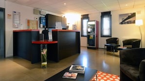 A reception area with a desk, chairs, a vase with flowers, and a coffee table with magazines. - Hôtel Inn Dijon-Quetigny (Quetigny)