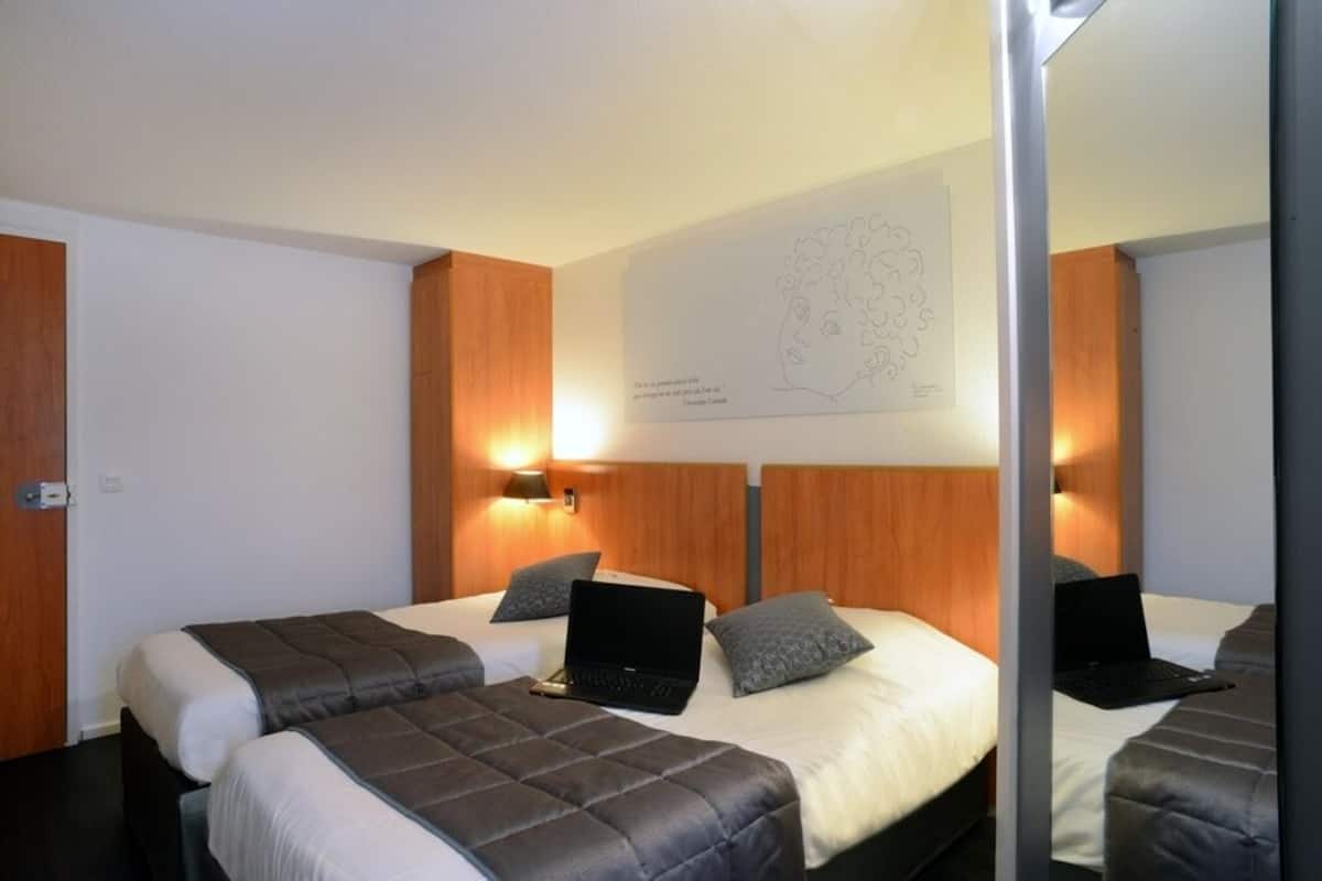 A hotel room with two beds, each with a laptop and pillows. There is a wall-mounted artwork above the beds.