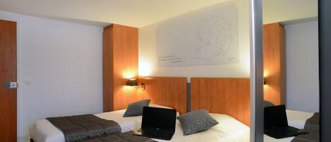 Habitación de hotel con dos camas, cada una con una laptop y almohadas. Hay una obra de arte colgada en la pared sobre las camas.