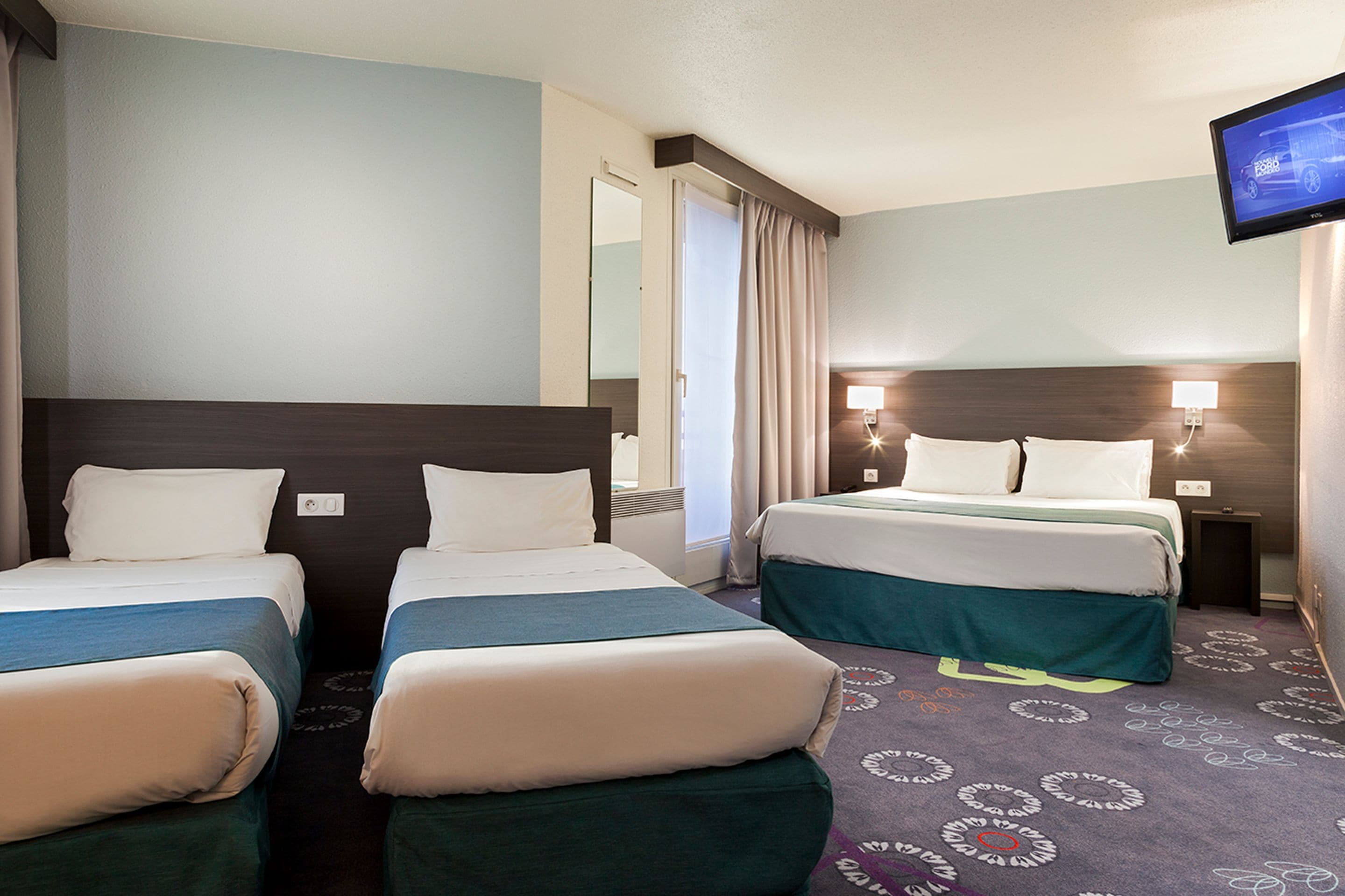 A hotel room with two beds, a television, and a bathroom visible through an open door.