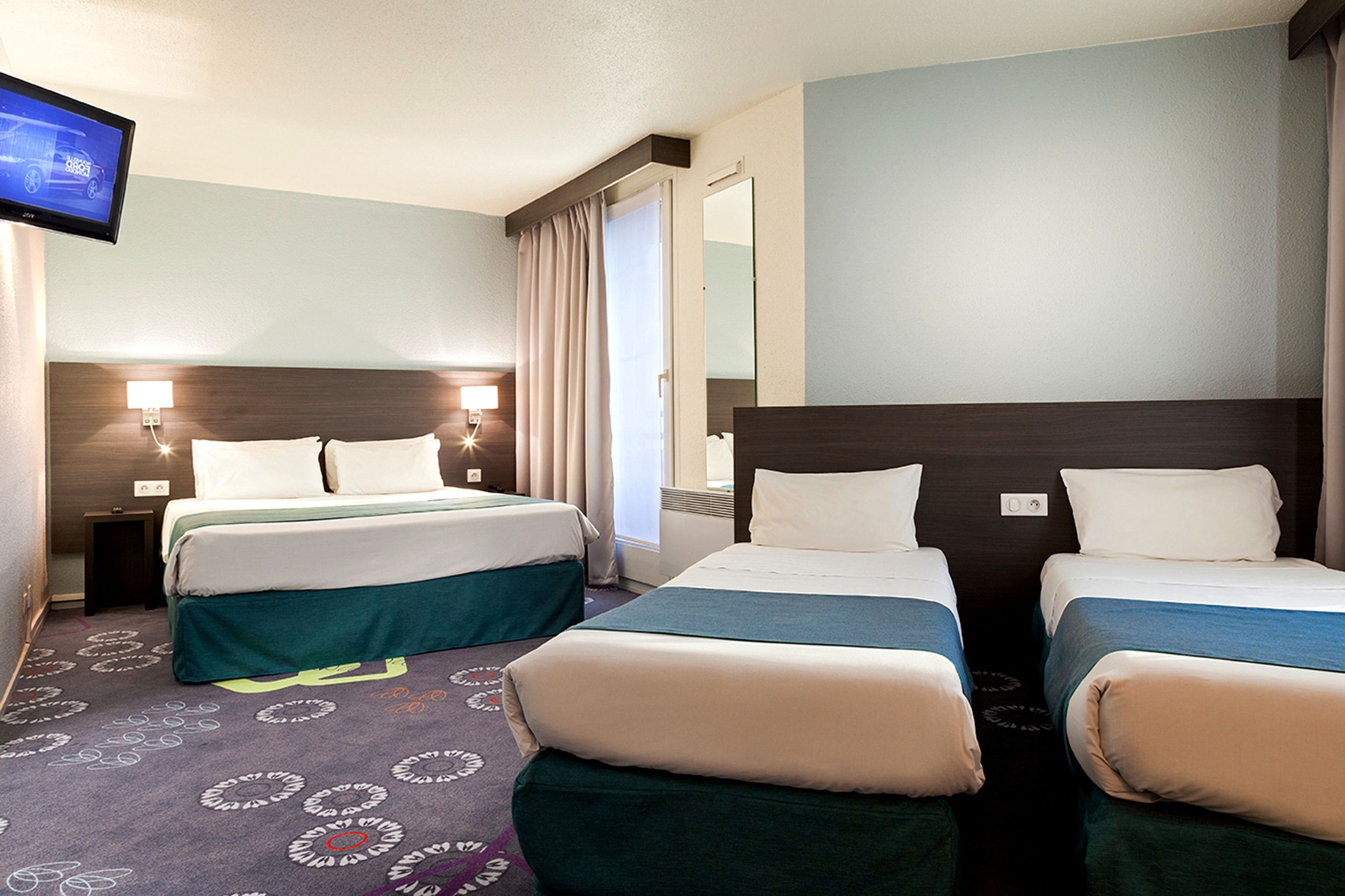 A hotel room with two beds, a television, and a mirror.