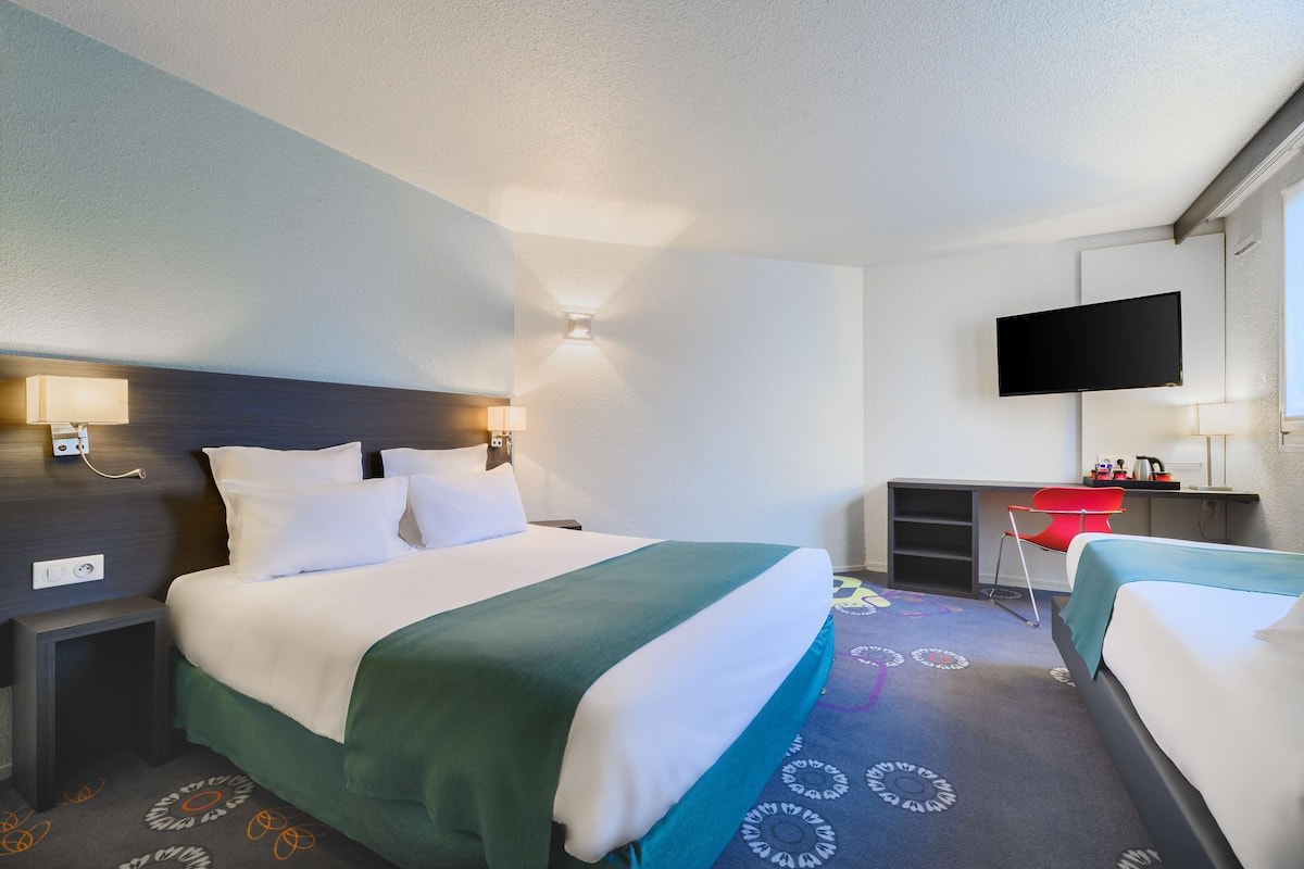 A hotel room with a bed, a desk, a TV, and a chair.