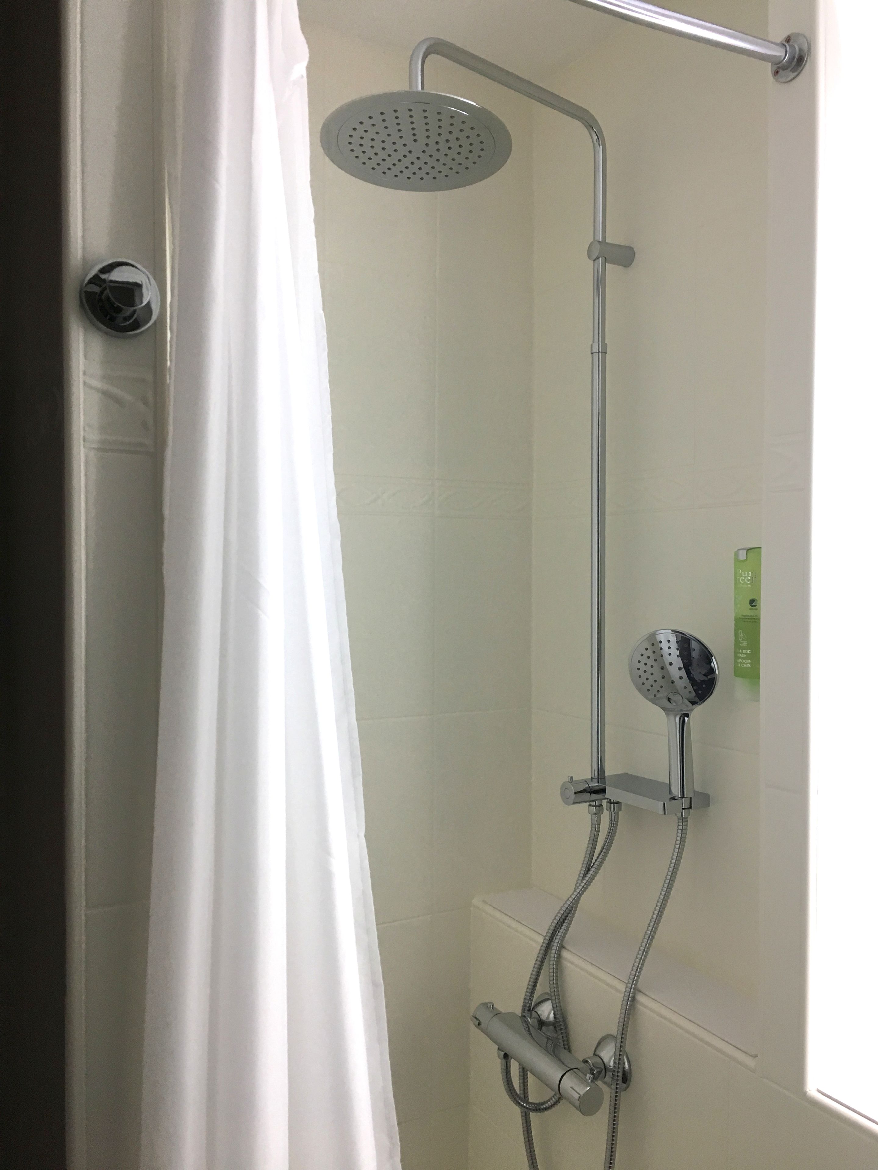 A shower with a handheld showerhead and a wall-mounted showerhead, both with hoses.