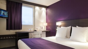 Een hotelkamer met een bed, een bureau, een televisie en een raam met gordijnen.
