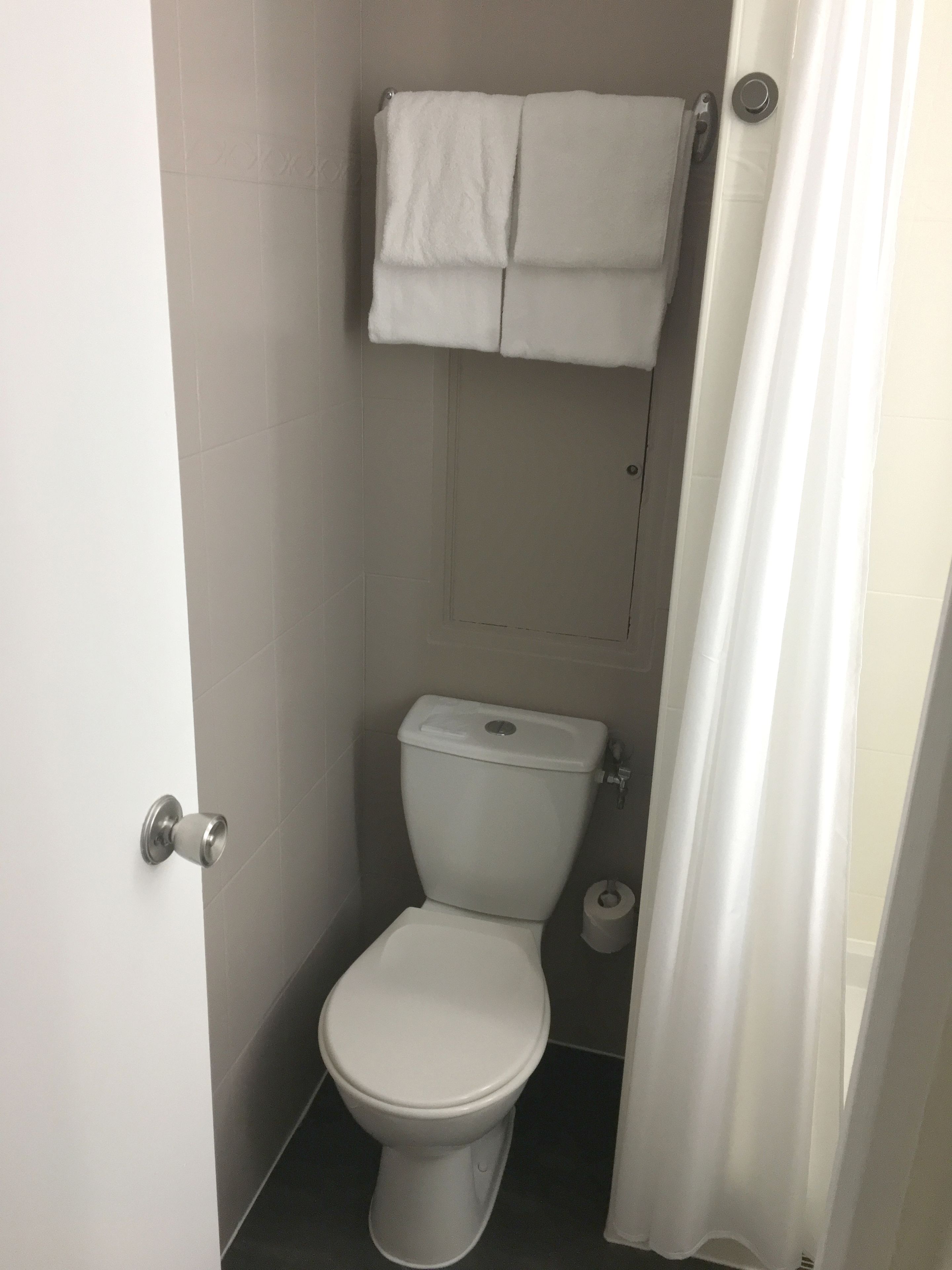 A small, clean bathroom with a toilet, a towel rack above the toilet, and a toilet paper holder.