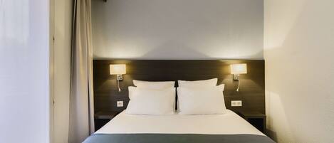 A hotel room with a large bed, two bedside lamps, and a window with curtains.