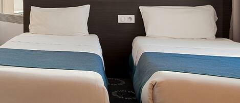 A hotel room with two single beds, each with a white pillow and a blue bedspread.