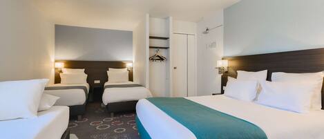 A hotel room with two beds, a wardrobe, a mirror, and a small seating area.