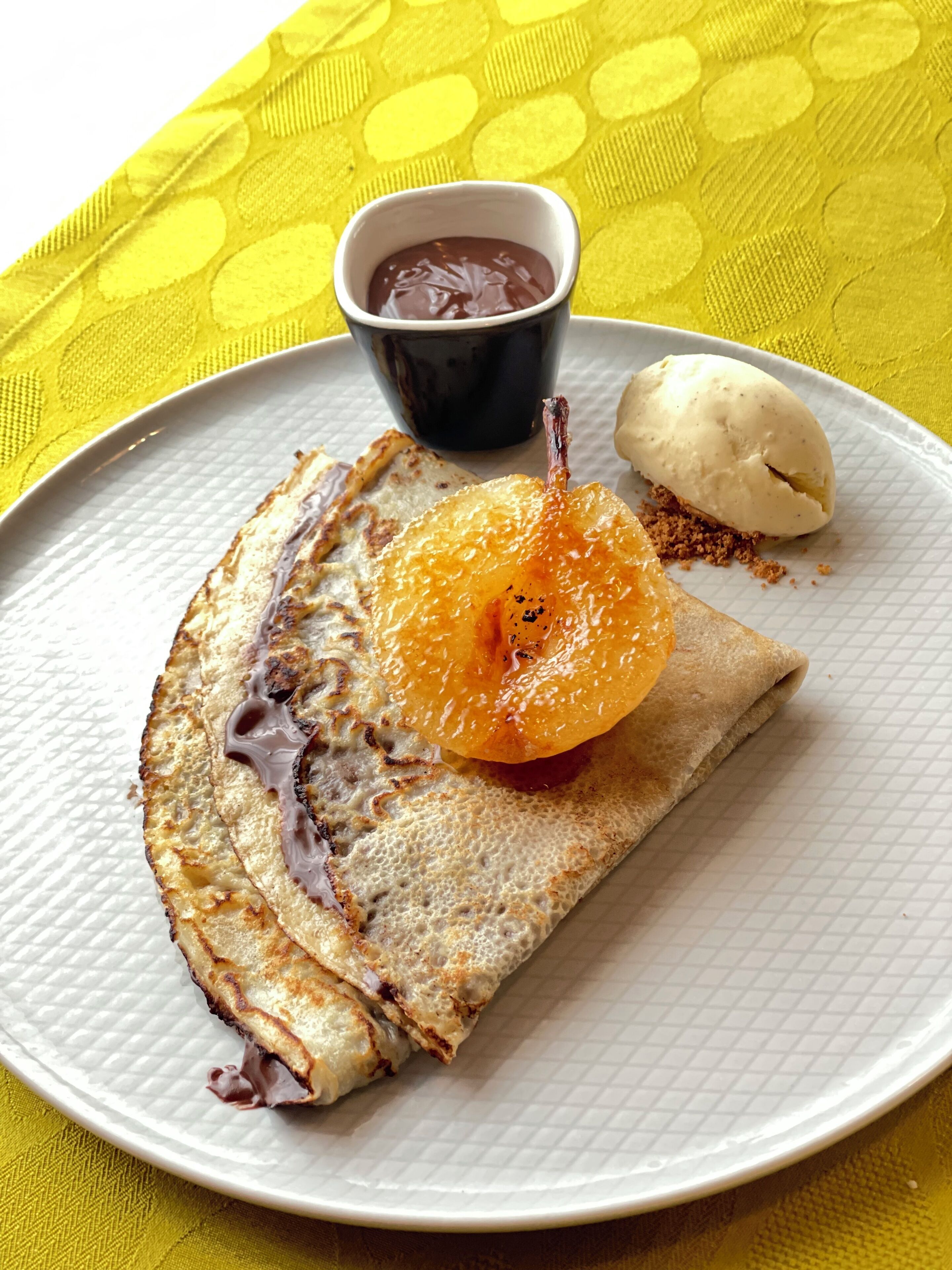 A plate with a crepe, a scoop of ice cream, and a small bowl of chocolate sauce.