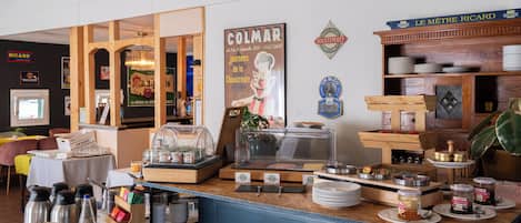 A breakfast bar with a variety of food items and condiments, a poster of a chef, and a sign for 'Le Maitre Ricard' wine.