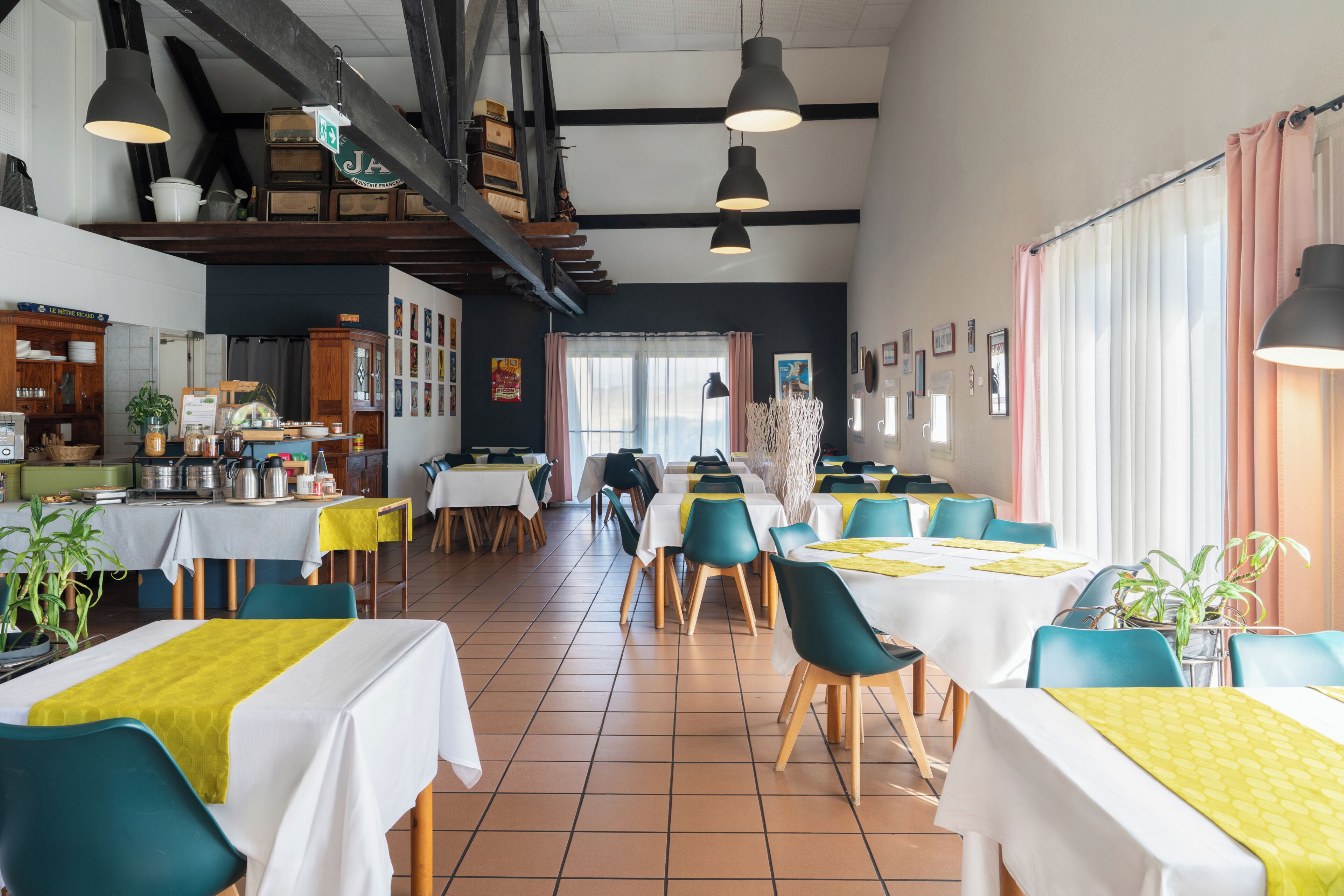 Um restaurante com várias mesas e cadeiras, uma área de cozinha e um lance de escadas.