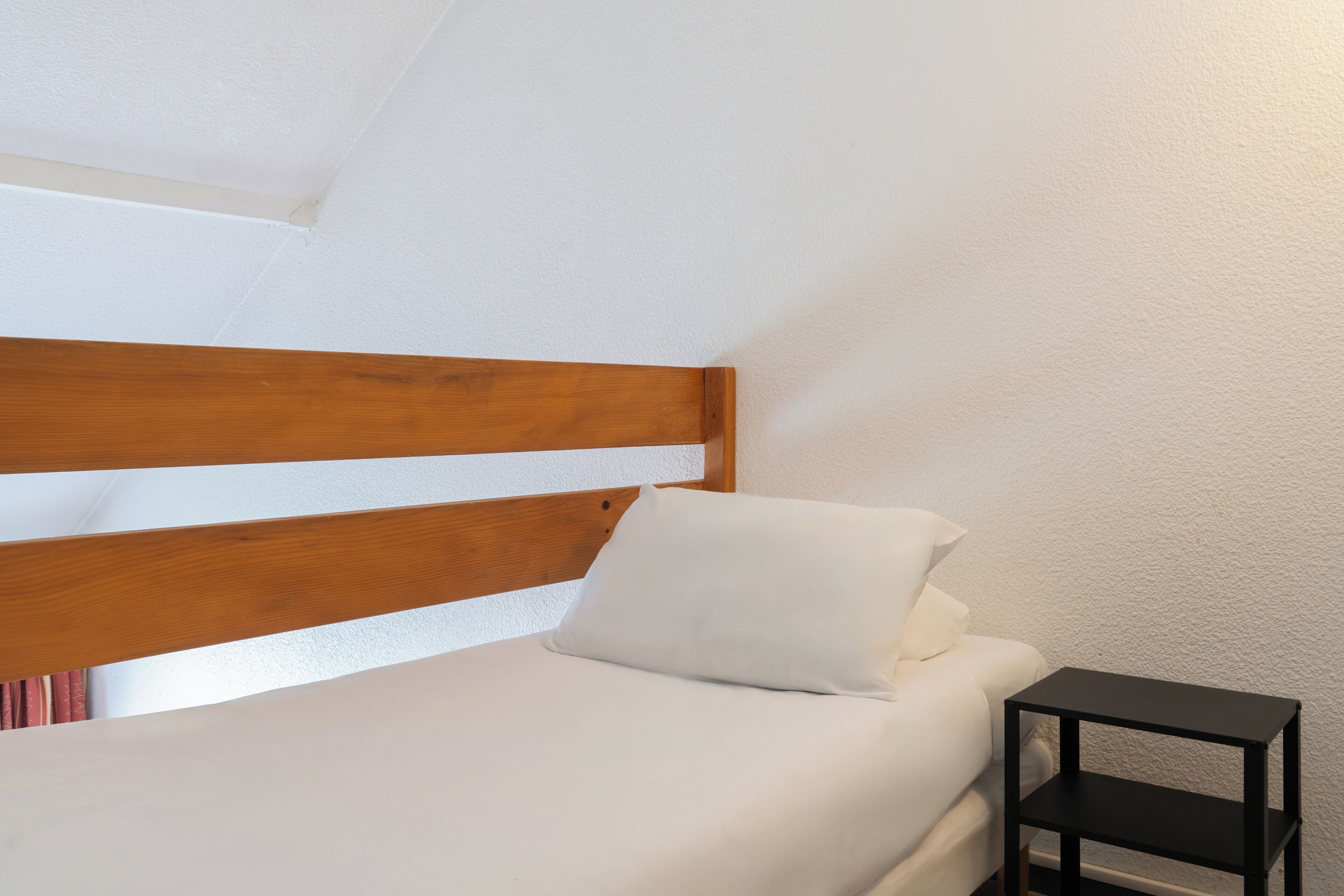 Ein Schlafzimmer mit einem Holzkopfteil, einer weißen Matratze und einem Nachttisch in Schwarz.