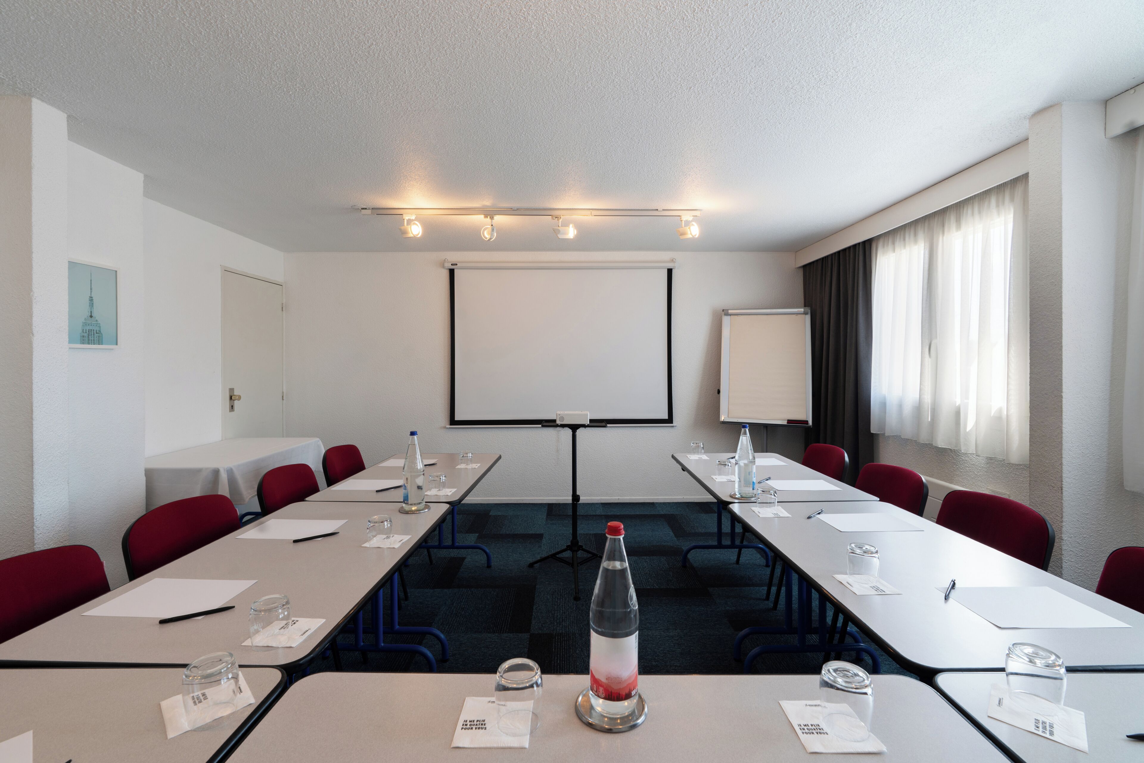 Une salle de conférence équipée d’une longue table, de chaises, d’un écran de projection et d’un tableau blanc.