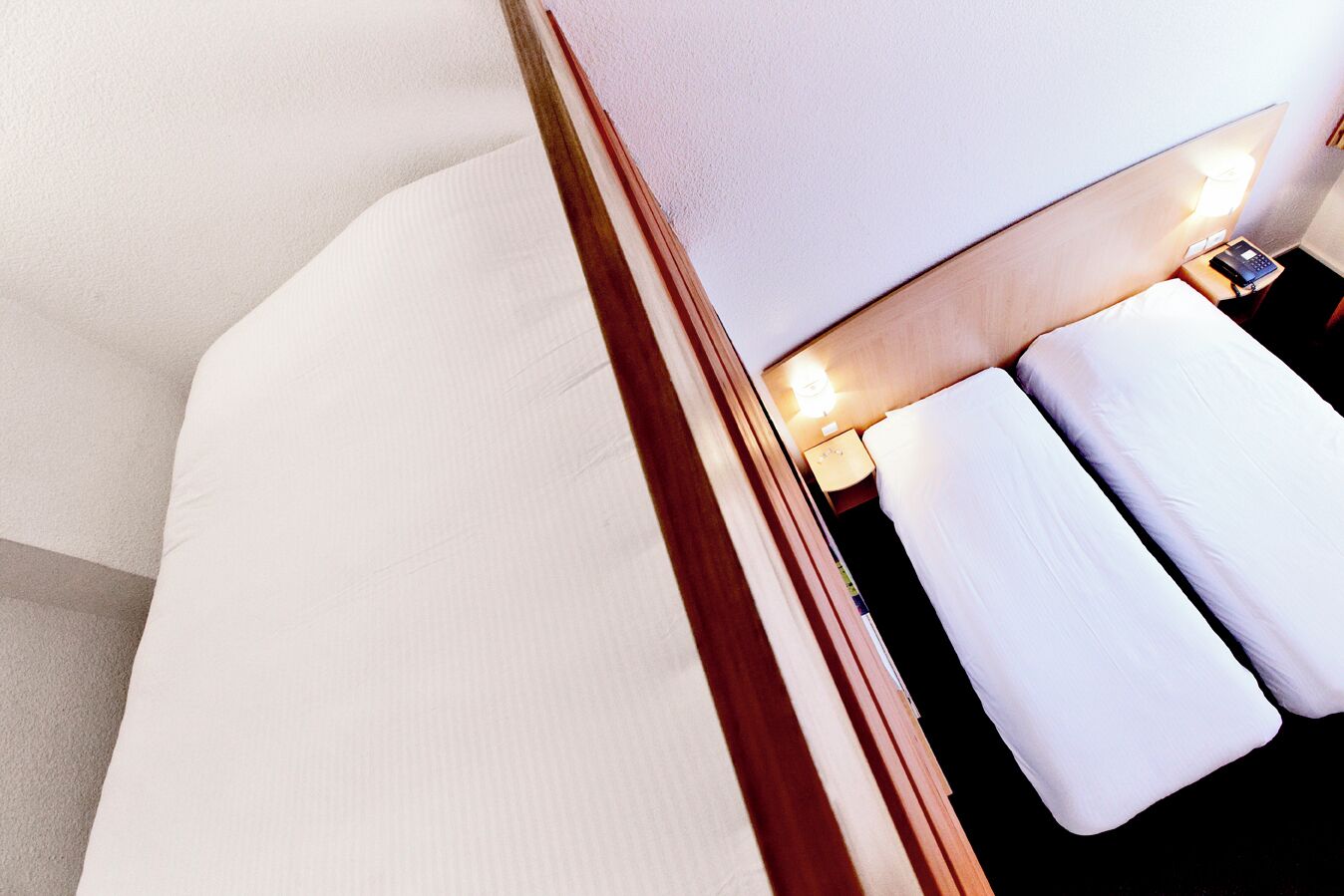 A modern hotel room with a neatly made bed, a bedside table with a lamp, and a small nightstand with a phone.
