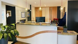 A reception area with a curved counter, a large screen, and a potted plant. - Hotel La Maison de Lise Mulhouse Illzach (Illzach)