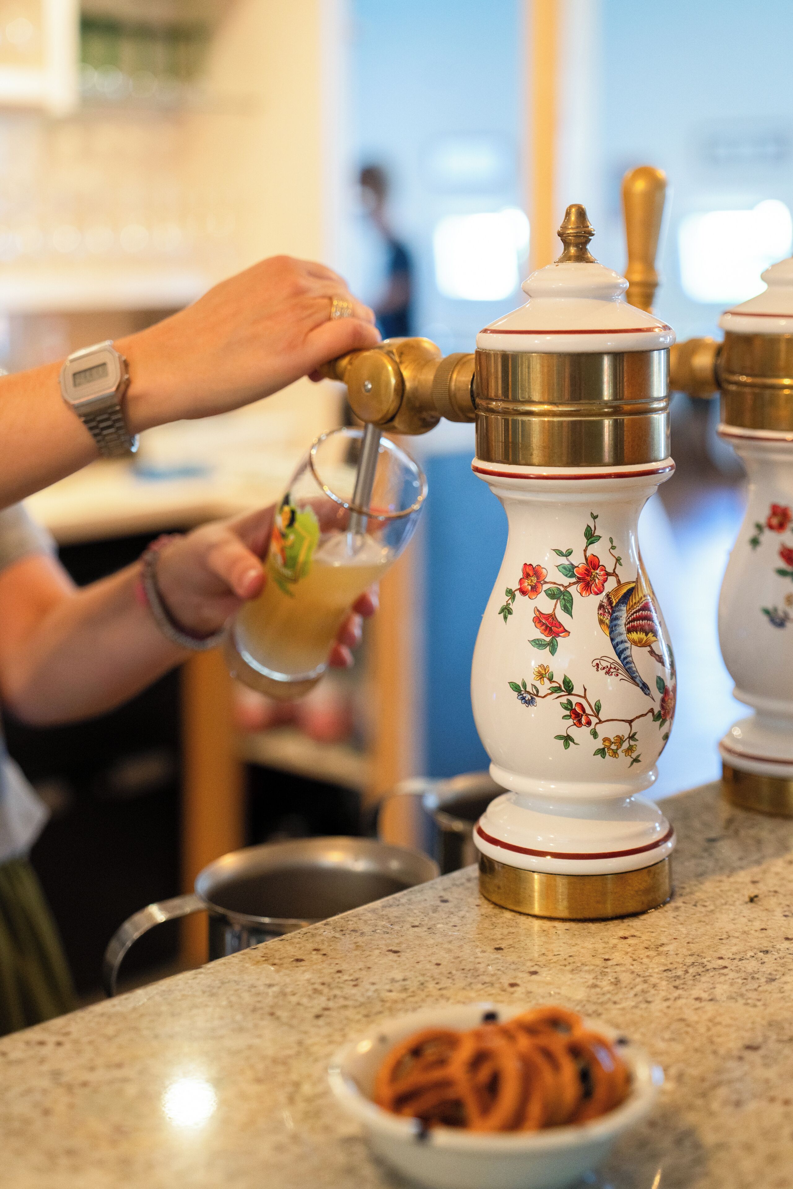 En person betjener en manuel espressomaskine, med en skål kaffebønner og et glas kaffe på disken.
