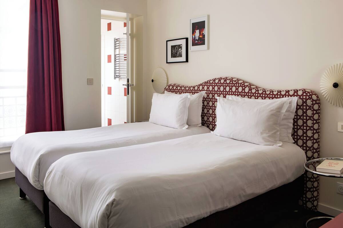 A hotel room with two beds, a patterned headboard, a bedside table with a lamp, and a door with a view of the outside.