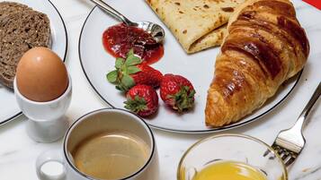 A breakfast setting with croissants, strawberries, jam, a boiled egg, and coffee on a marble table.