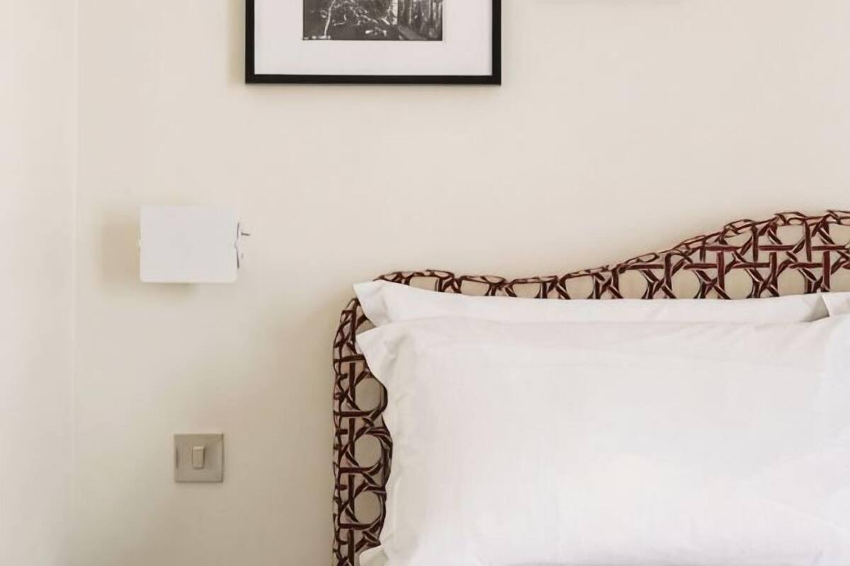 A bed with a patterned headboard, a white pillow, a framed picture on the wall, and a light switch.
