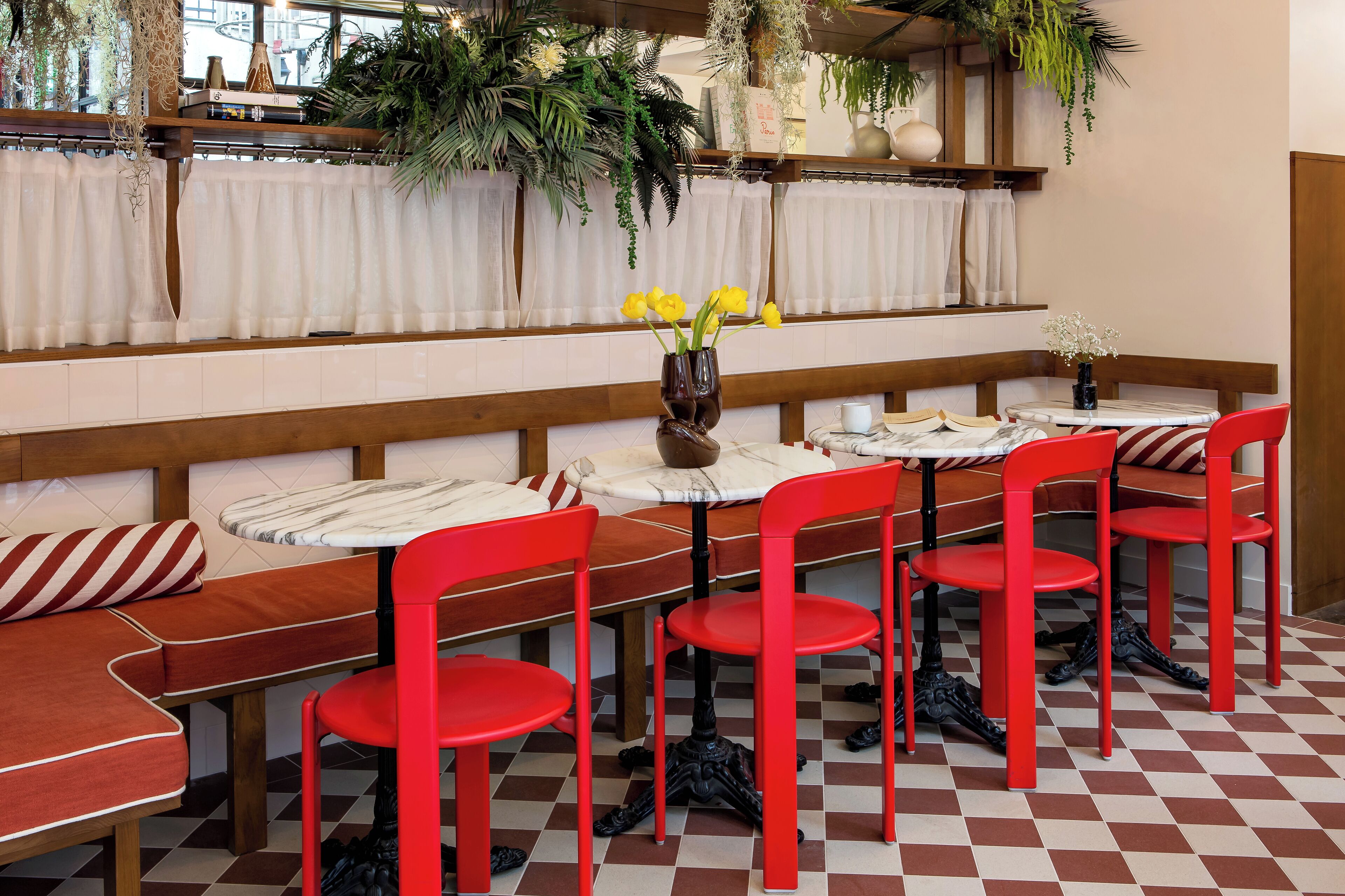 Interior de restaurante con sillas rojas, cortinas blancas y suelo a cuadros.