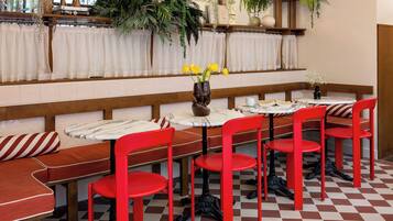 Interior de restaurante con sillas rojas, cortinas blancas y suelo a cuadros.