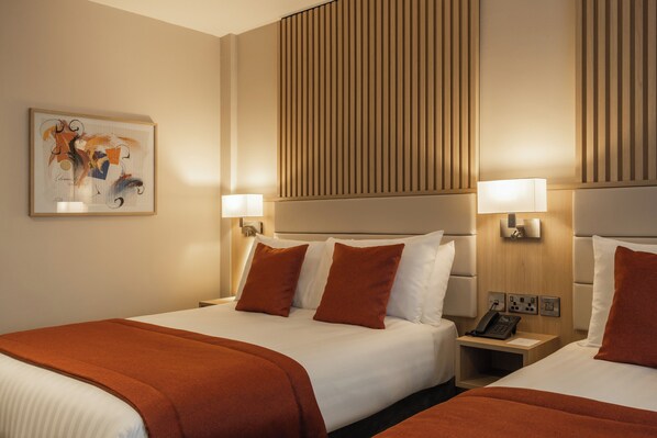A hotel room with two beds, a headboard with vertical lines, bedside lamps, a framed artwork on the wall, and a phone on the nightstand. - Da Vinci's Hotel Derry (Londonderry)