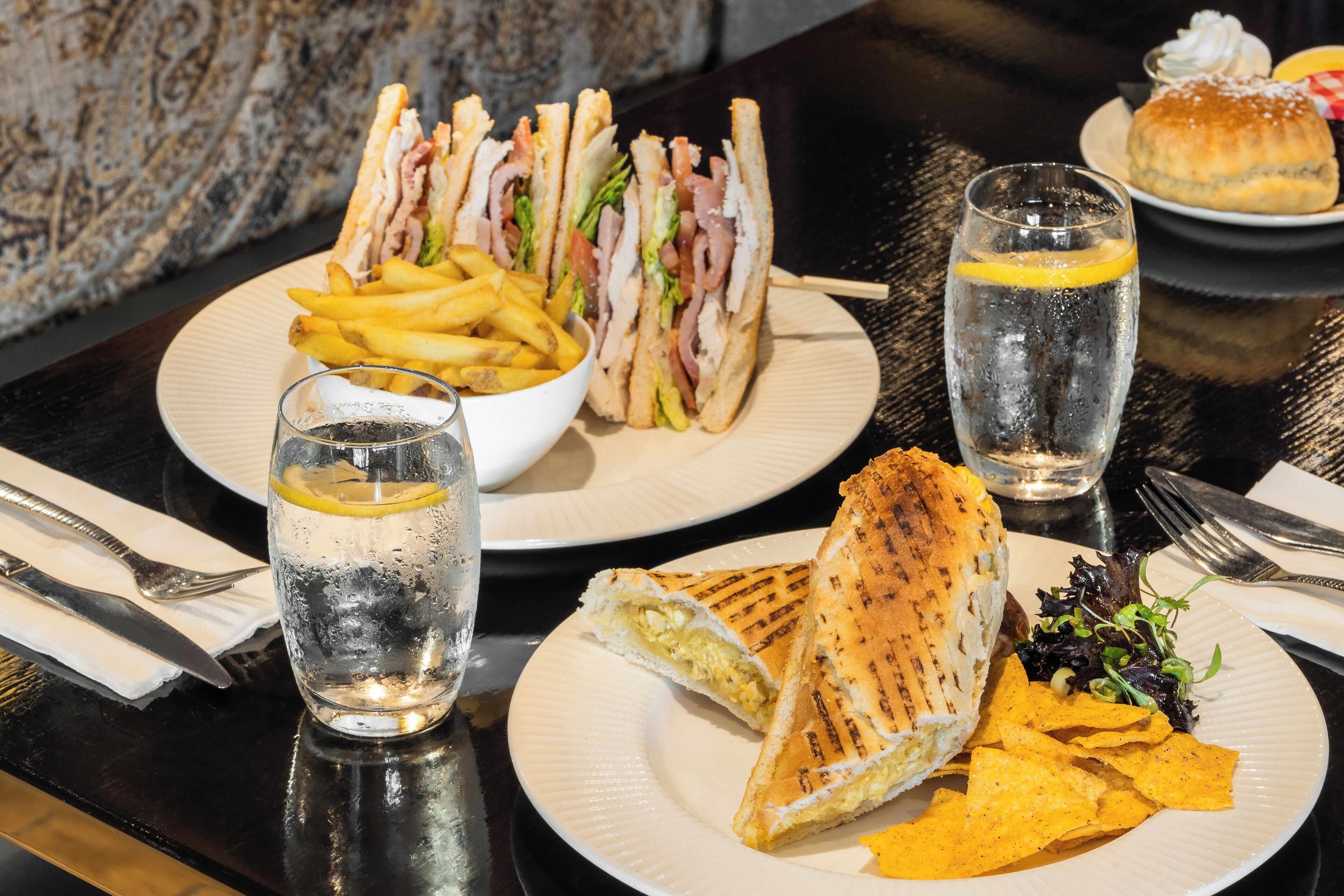 A table with a sandwich, fries, chips, a glass of water, and a dessert plate.