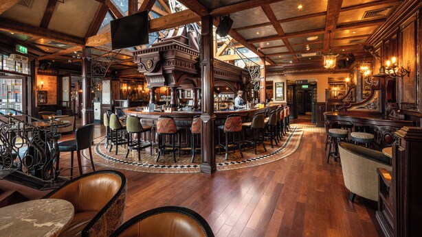 A bar area with wooden beams, a bar counter, and multiple seating arrangements including bar stools and chairs. - Da Vinci's Hotel Derry (Londonderry)