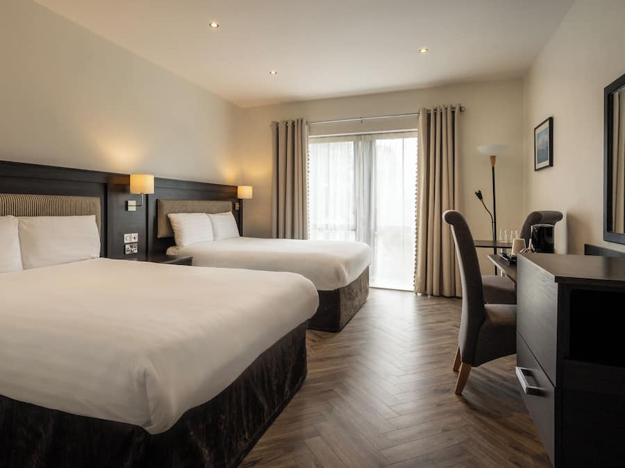 Habitación de hotel con dos camas, un escritorio, una silla, un televisor y un ventanal con cortinas.