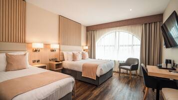 A hotel room with two beds, a desk, a chair, a TV, and a large window with curtains.