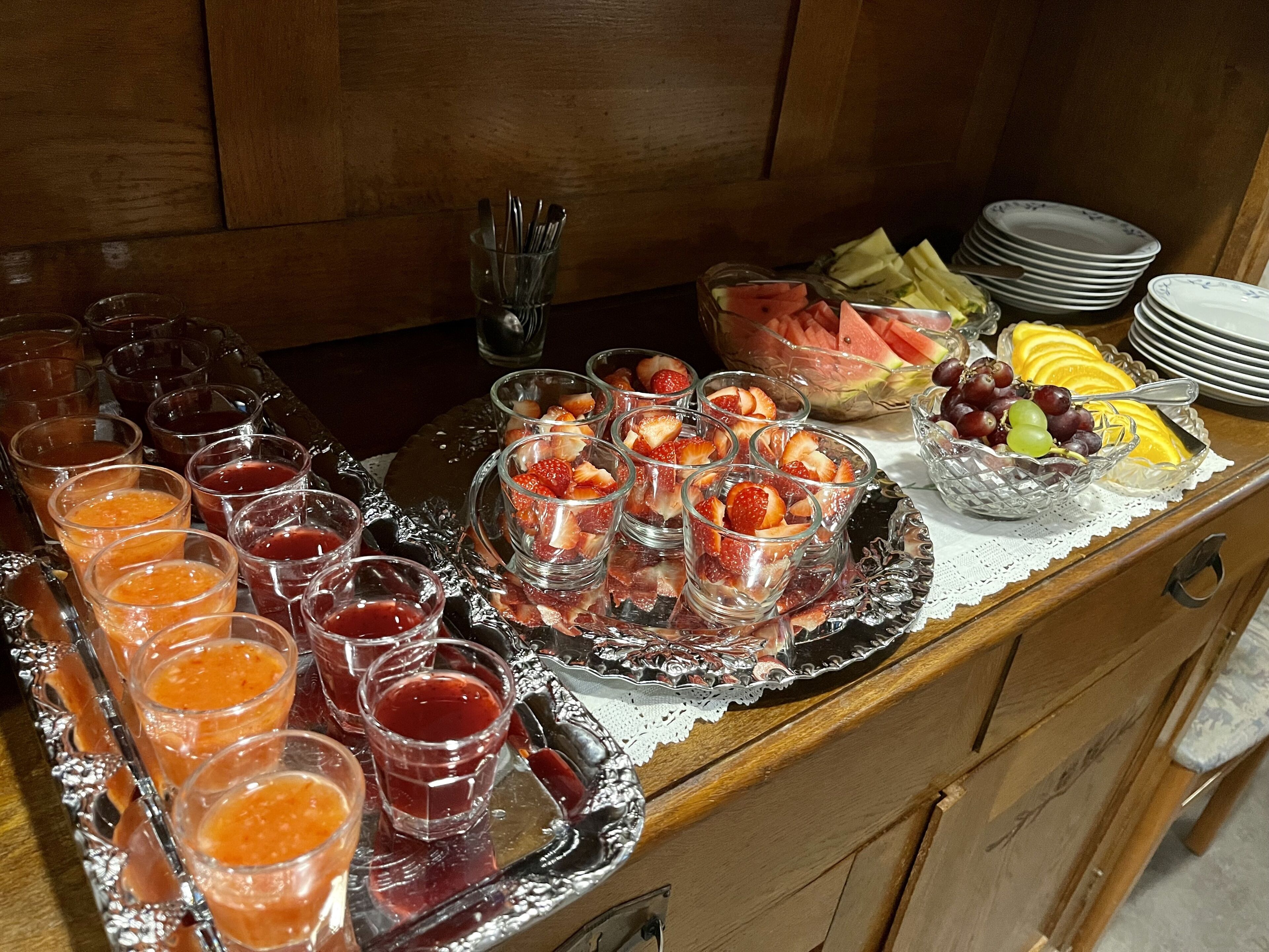 Una mesa de buffet con diversas frutas, frutas cortadas y vasos de jugo.
