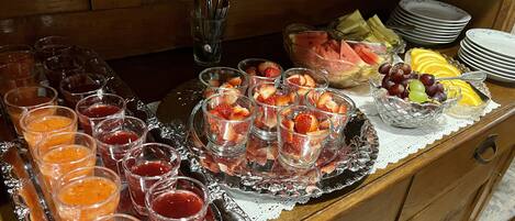 Una mesa de buffet con diversas frutas, frutas cortadas y vasos de jugo.