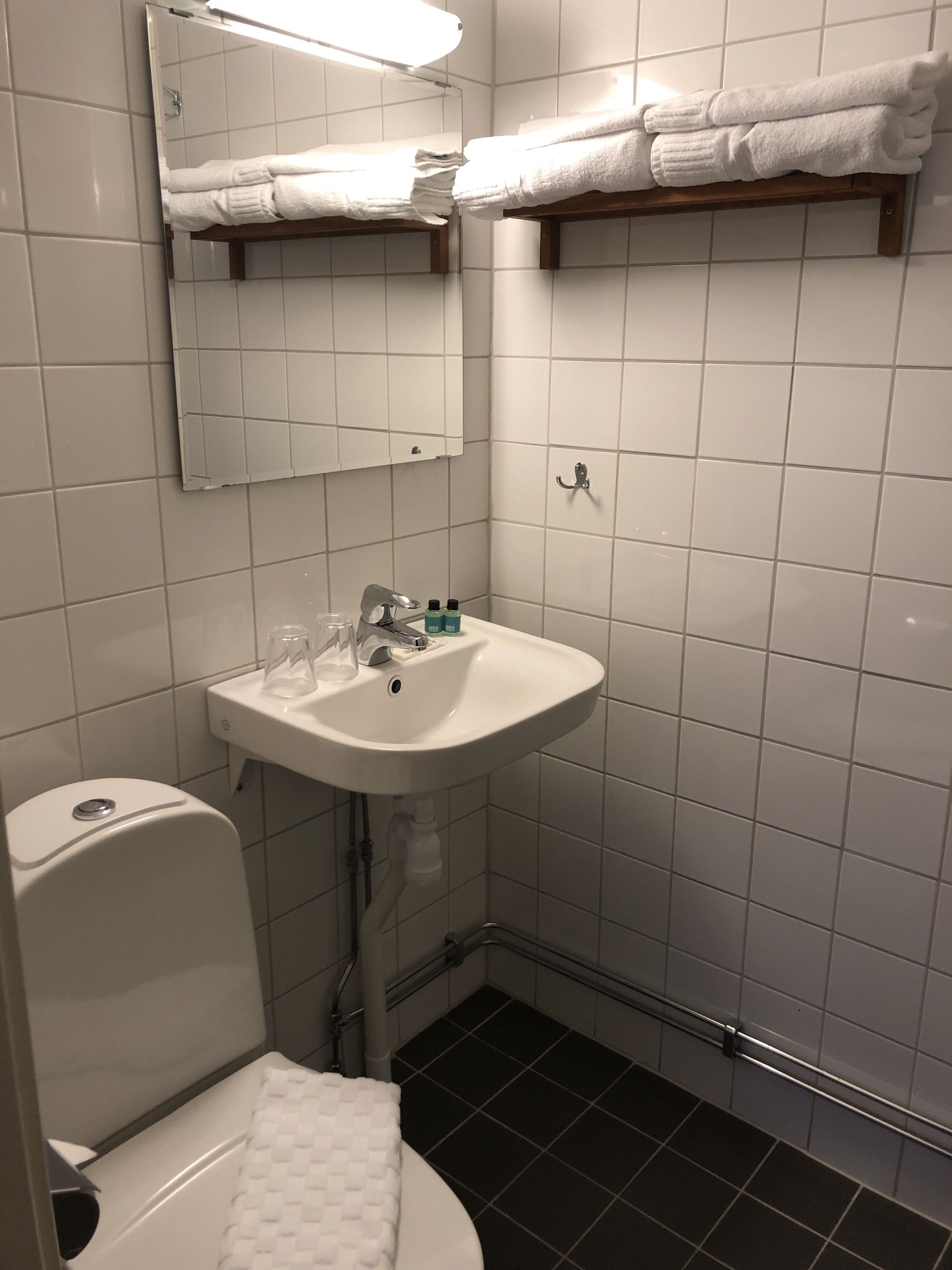 Un baño con un lavamanos blanco, un espejo y dos toalleros.
