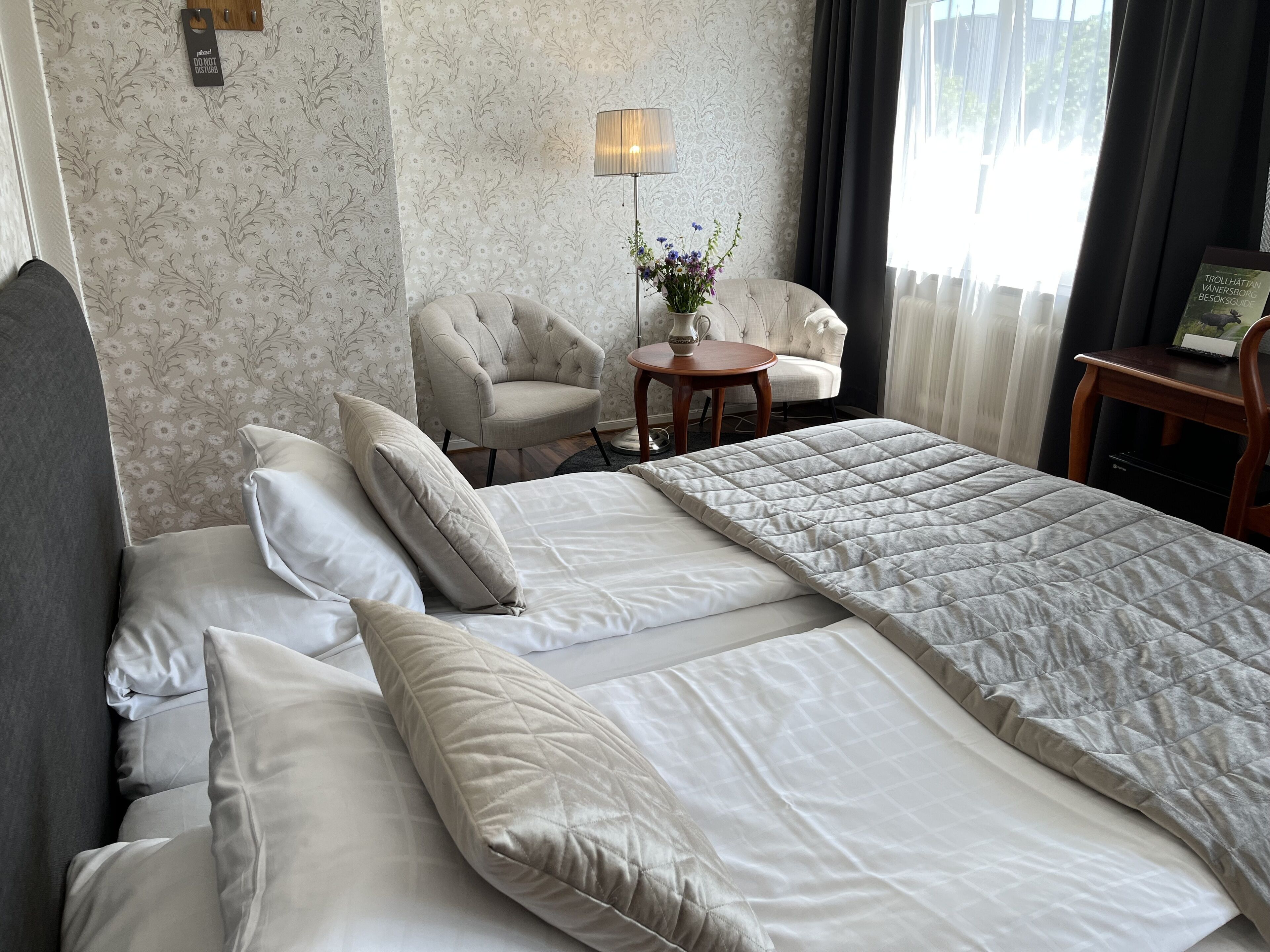 Et hotelværelse med en stor seng, to stole, et lille bord med en blomstervase og en lampe.