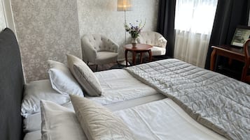 A hotel room with a large bed, two chairs, a small table with a vase of flowers, and a lamp.